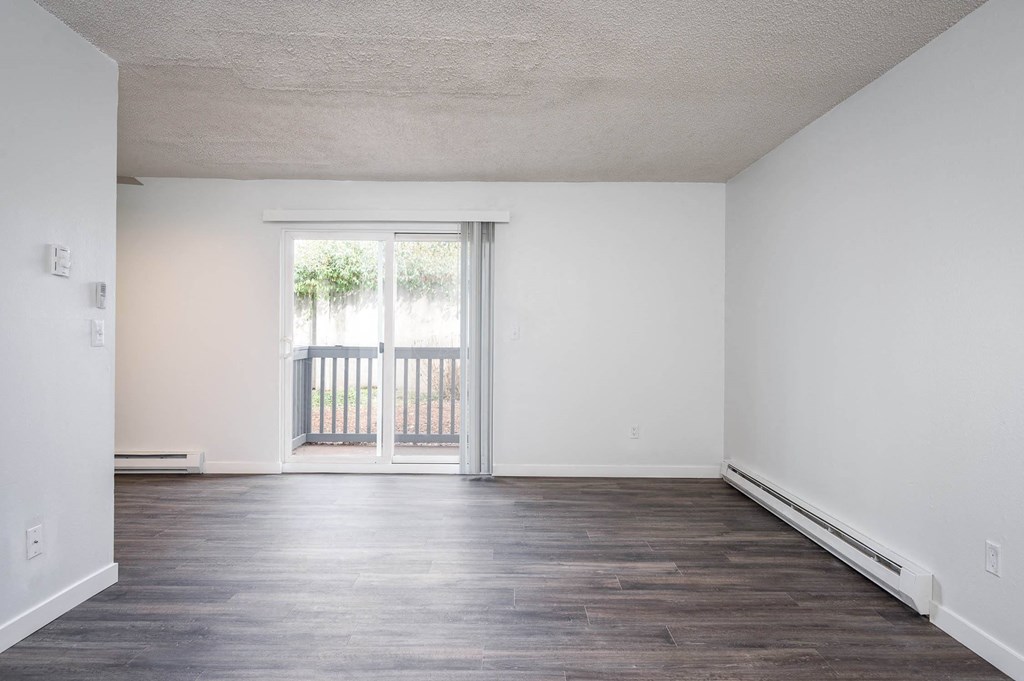 an empty living room with white walls and a door to a balcony
